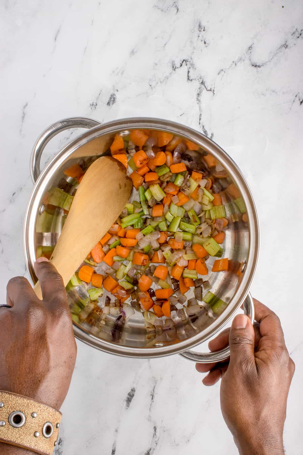 Hands mixing veggies in a cooking pot. 