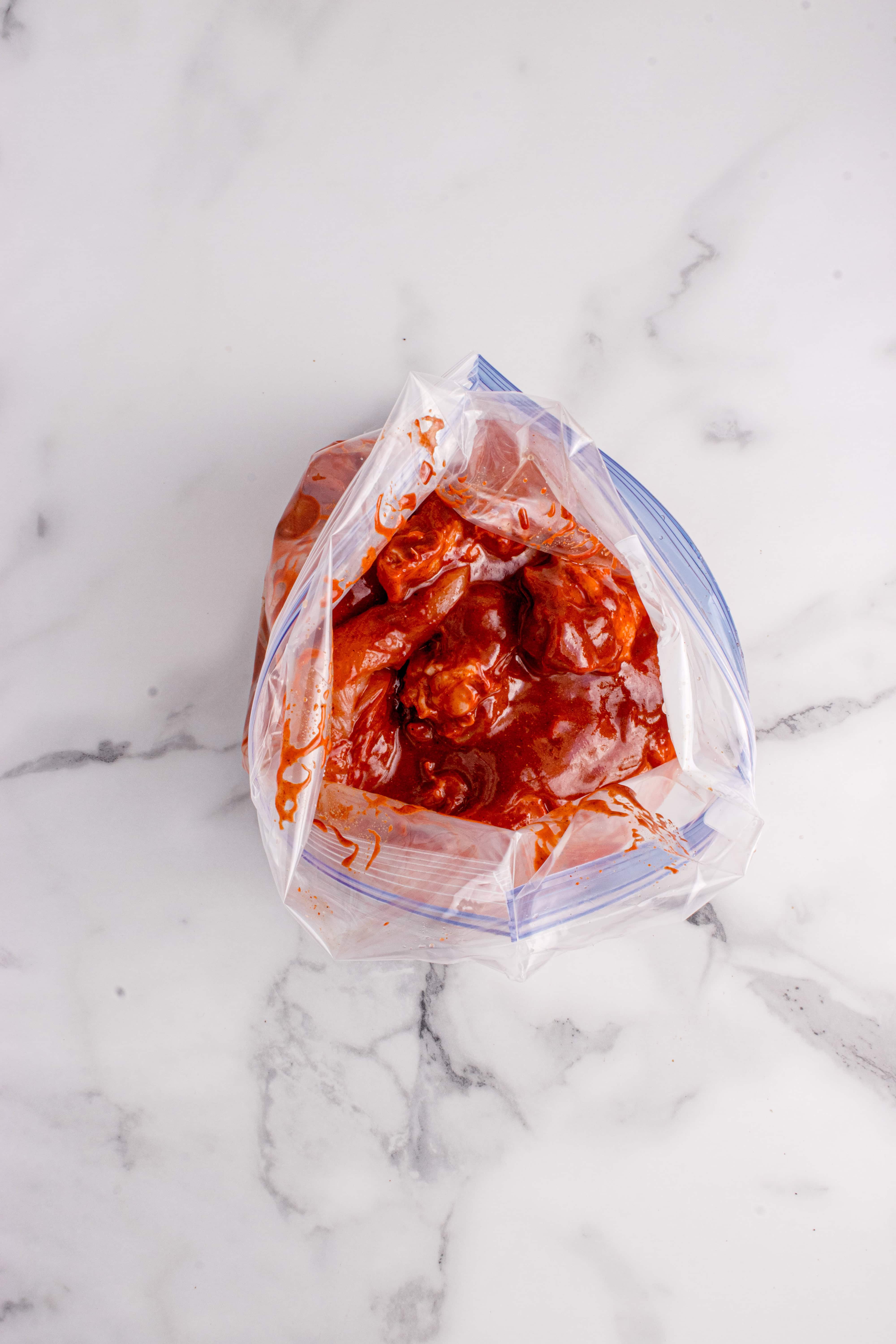 Marinade being poured over the chicken in a freezer bag