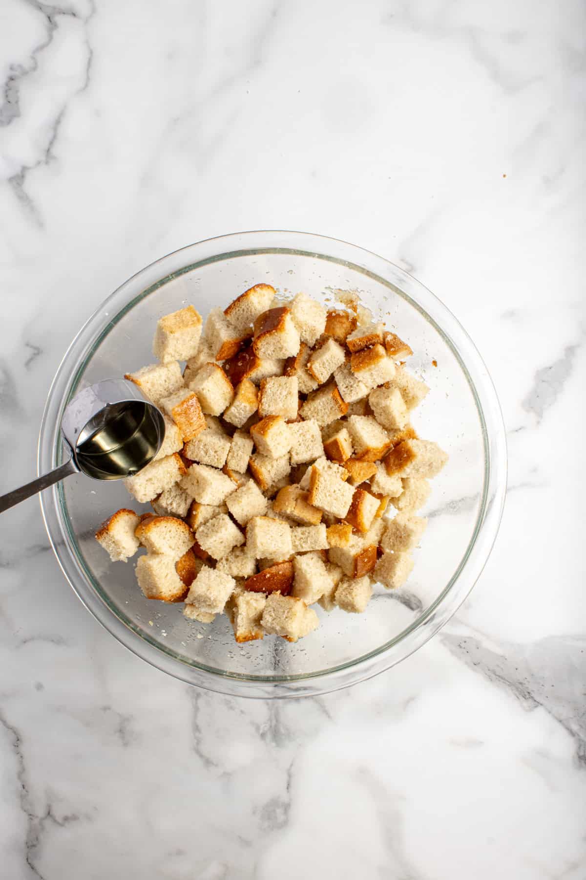 Oil being poured into cubed bread in a bowl