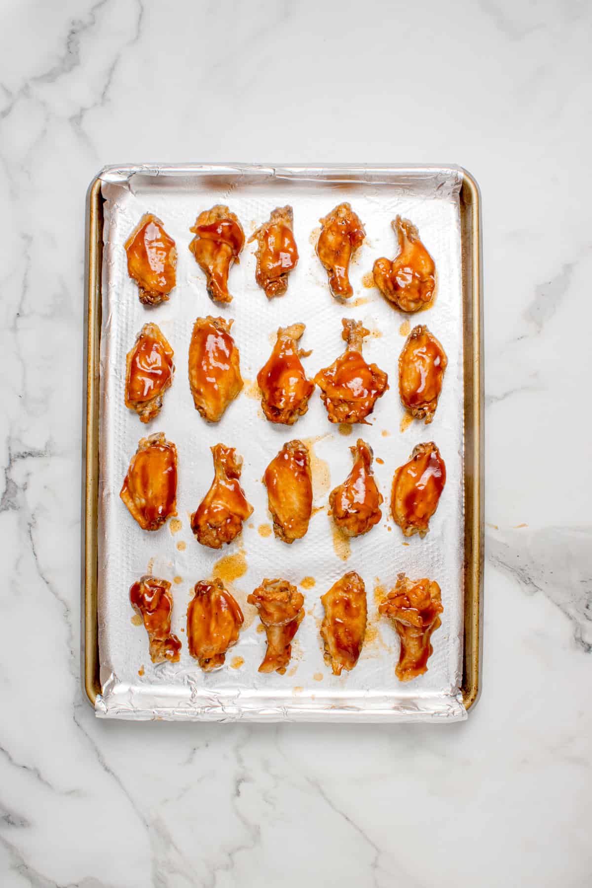 Slow cooked wings on a baking sheet with BBQ sauce brushed on them. 